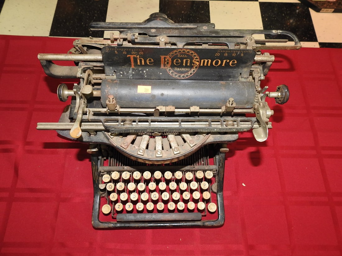 Antique Densmore Typewriter: Antique Densmore typewriter with black body, exposed type bars and round keys. Approx. 10 x 17.5 x 15.5 in. Keys appear to move, but carriage needs work; sold as a collectible/display typewriter with 