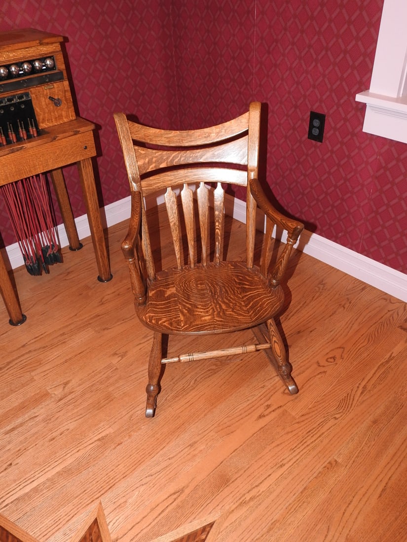 Antique Wooden Rocking Chair: Antique wooden rocking chair with shaped arms, slat back, curved runners, and warm oak-toned finish. Approx. 36 x 21 x 30 in. Shows finish wear, scuffs, and age-related wear consistent with use and