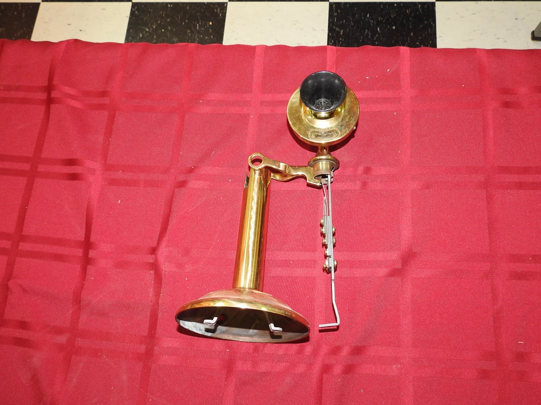 Brass Candlestick Telephone - Parts: Antique brass candlestick telephone with upright stem, flared base, black receiver/mouthpiece components, and cord/hook hardware. Maker not clearly visible. Shows tarnish, patina, scuffs, and age-rela