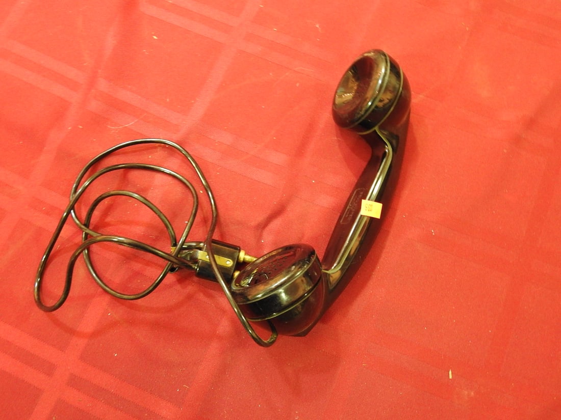 Western Electric F1 Style Handset: Antique black telephone receiver/handset with cloth cord and brass connector ends. Maker mark is present but not fully legible in photos. Shows scuffs, finish wear, cord wear, and age-related