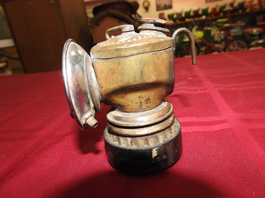 Antique Brass Carbide Lamp: Antique brass carbide/miner-style lamp with reflector, hook hardware, vented base, and top lever/screw details. Maker not clearly visible in photos. Shows tarnish, oxidation, dents, finish wear, and a