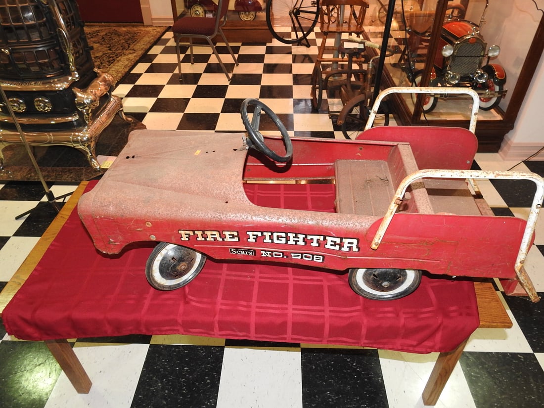 Fire Fighter Sears No. 508 Pedal Car: Vintage Fire Fighter pedal car, license plate JW 2580, with red body and fire graphics. Approx. 19 x 16 x 46 in. Missing ladders; seat area has rust as shown. Shows paint wear, oxidation, surface scra