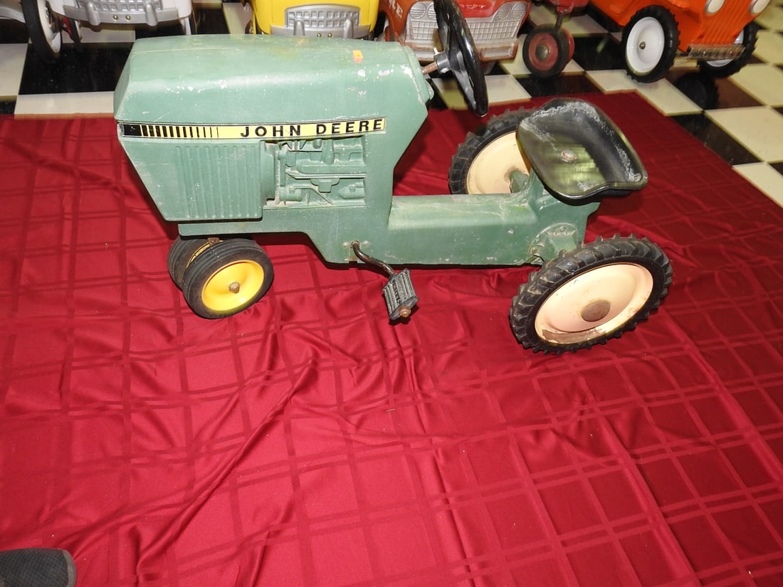 Vintage John Deere Pedal Tractor: Vintage John Deere pedal tractor with green body, yellow wheels and metal seat. Approx. 24 x 20 x 35 in. Shows paint wear, scratches, oxidation, tire wear and age-related use wear; see photos for