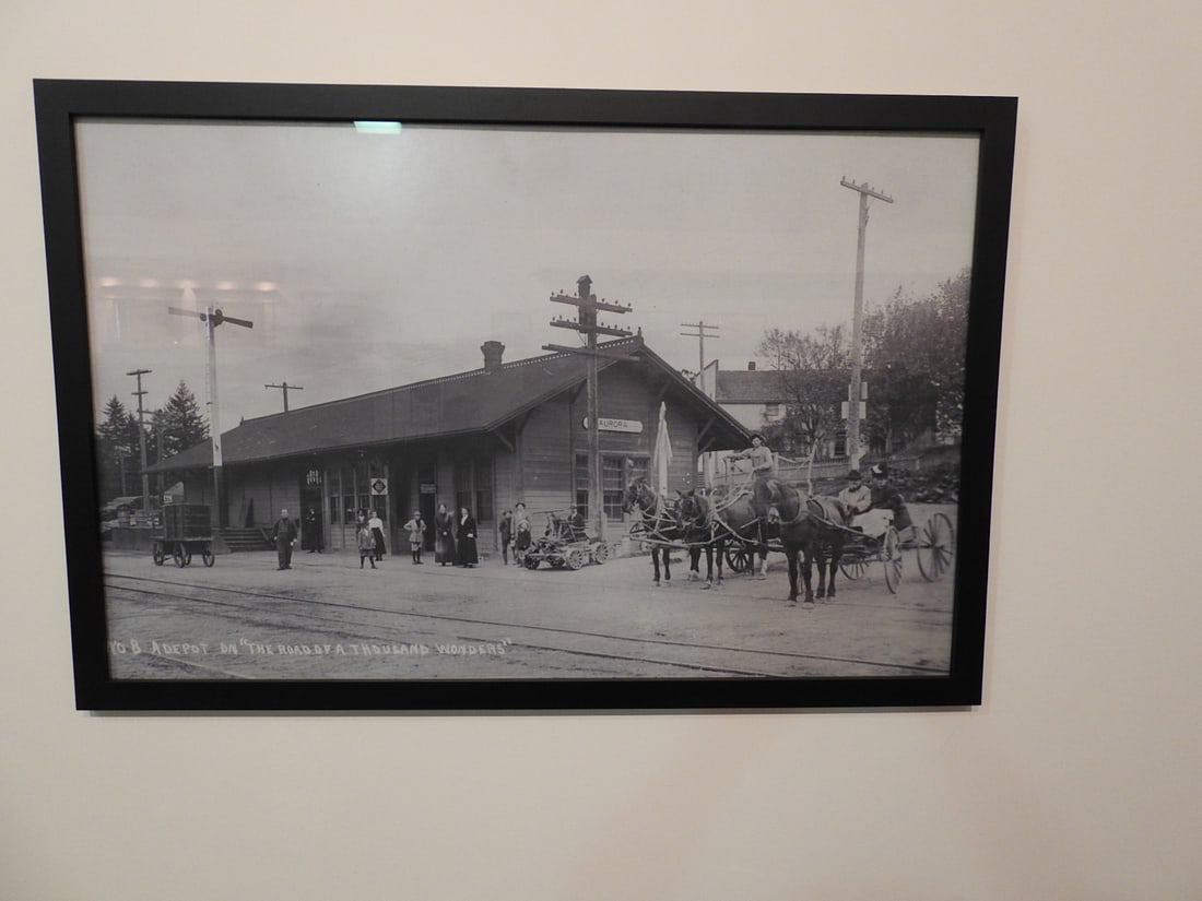 Framed Road of a Thousand Wonders Depot, Aurora OR Photo: Framed black-and-white historical photograph/print titled The Road of a Thousand Wonders, Depot, Aurora, Oregon. Approx. 25.5 x 29 x 1 in. Frame and print show age/display wear, surface marks, dust an