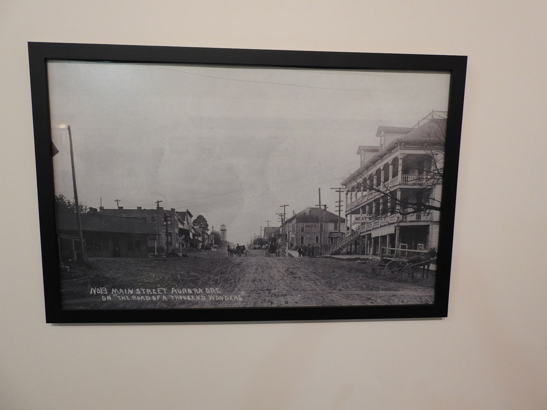 Framed Road of a Thousand Wonders Main St, Aurora OR Photo: Large framed black-and-white historical photograph/print titled The Road of a Thousand Wonders, Main St., Aurora, Oregon. Approx. 25 x 37.5 x 1 in. Frame and print show age/display wear, surface marks