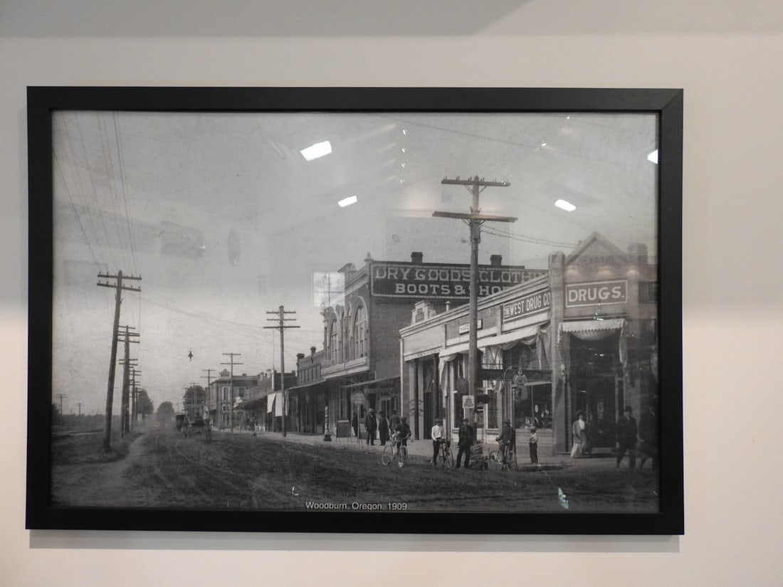 Framed Woodburn, Oregon 1909 Photograph: Large framed black-and-white Woodburn, Oregon 1909 historical photograph/print with early street or town scene. Approx. 26 x 38 x 1 in. Frame and print show age/display wear, surface marks, dust and b