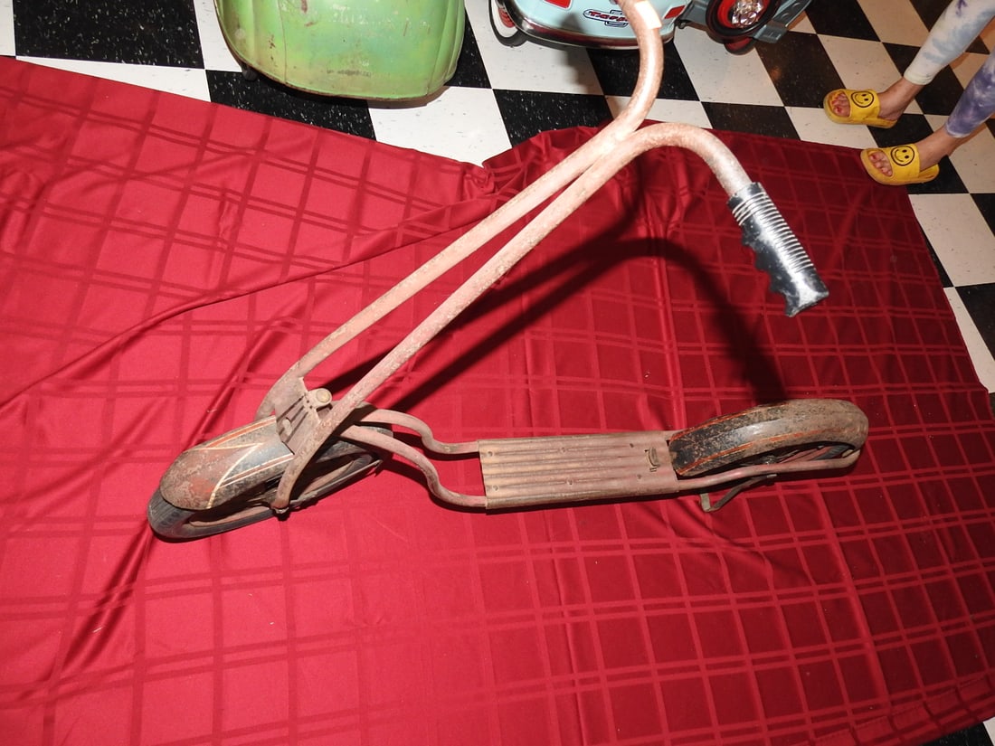 Vintage Red Kick Scooter: Vintage red kick scooter with metal frame, footboard, handlebar assembly and black wheels. Approx. 34 x 13 x 46 in. Shows age/use wear including paint loss, scratches, oxidation, tire wear and