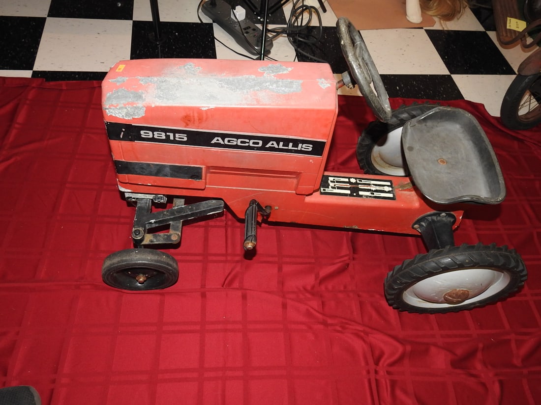 AGCO Allis 9815 Pedal Tractor: AGCO Allis 9815 pedal tractor with orange styling, metal body, steering wheel, seat and pedal drive. Approx. 25 x 20 x 38 in. Shows age/use wear, paint loss, scratches, oxidation, tire wear and patina