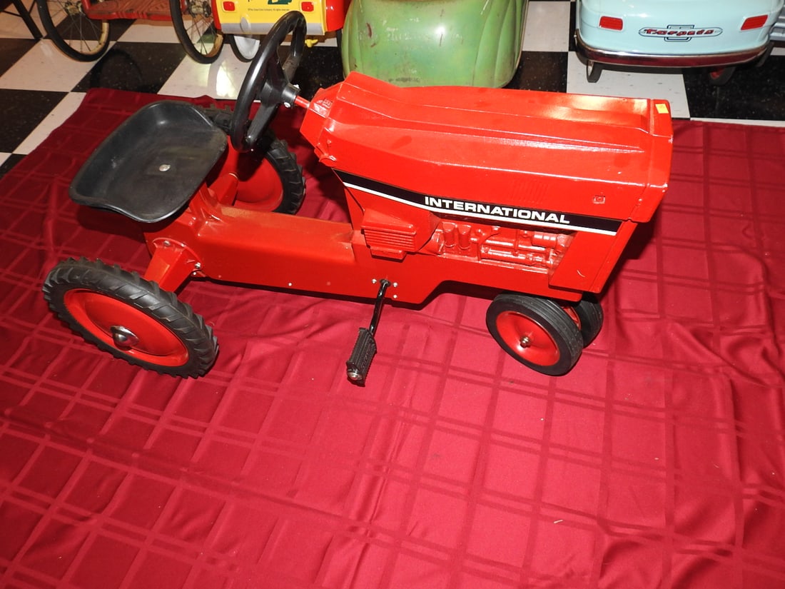 International Harvester Pedal Tractor: International Harvester pedal tractor with red styling, metal body, steering wheel, seat and pedal drive. Approx. 24 x 20 x 40 in. Shows age/use wear, paint loss, scratches, oxidation, tire wear and