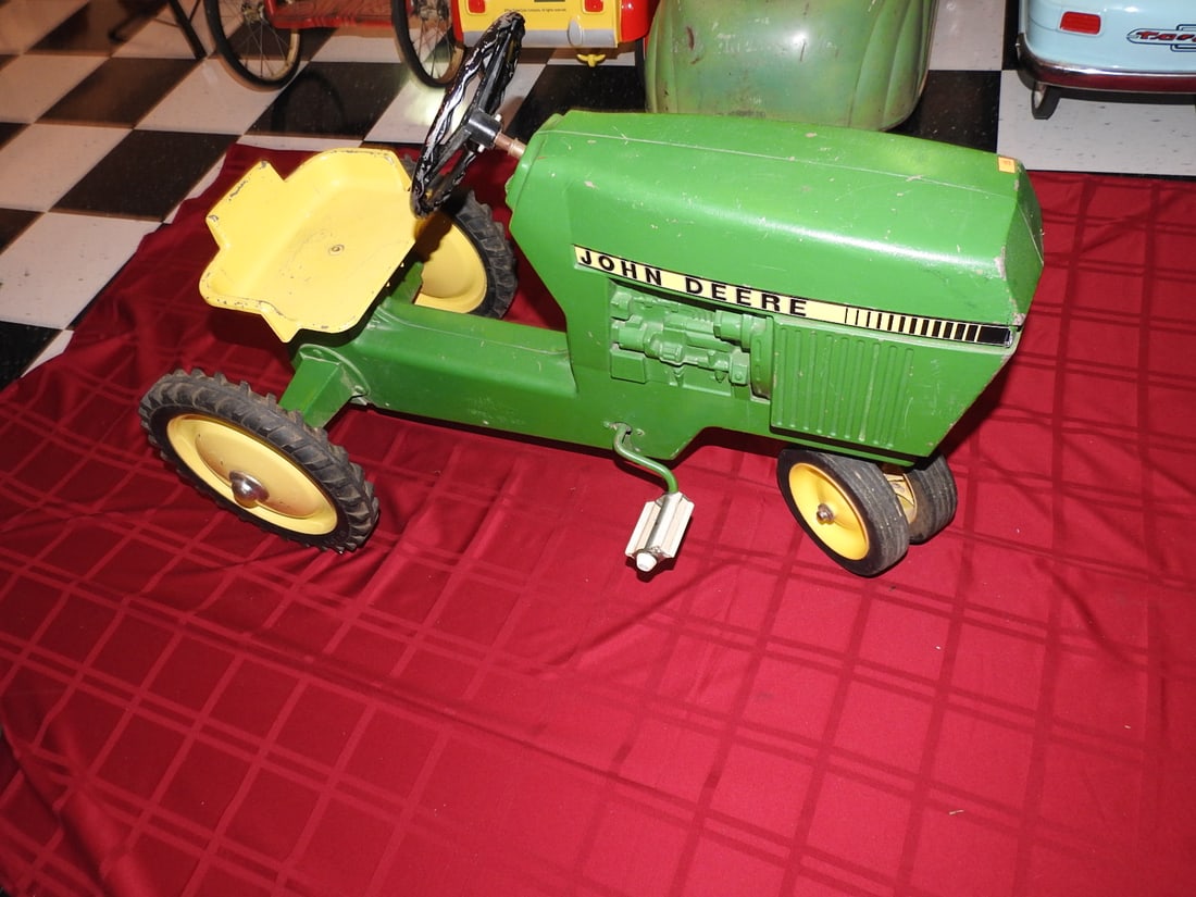 Vintage John Deere Pedal Tractor: Vintage John Deere pedal tractor with green and yellow styling, metal body, steering wheel, seat and pedal drive. Approx. 25 x 20 x 38 in. Shows age/use wear, paint loss, scratches, oxidation, tire