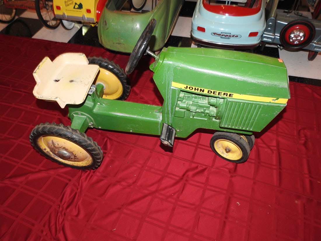 Vintage John Deere Pedal Tractor: Vintage John Deere pedal tractor with green and yellow styling, metal body, steering wheel, seat and pedal drive. Approx. 25 x 20 x 38 in. Shows age/use wear, paint loss, scratches, oxidation, tire