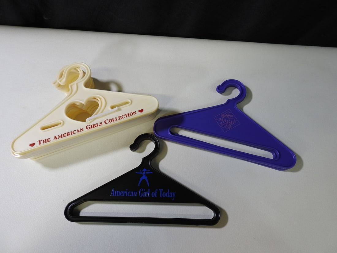 Lot of 13 American Girl-Style Doll Hangers: Lot of 13 assorted doll clothing hangers, including American Girl of Today examples and mixed plastic hangers as shown. Measured as packed. Approx. 3 H x 7 W x 4 D in.