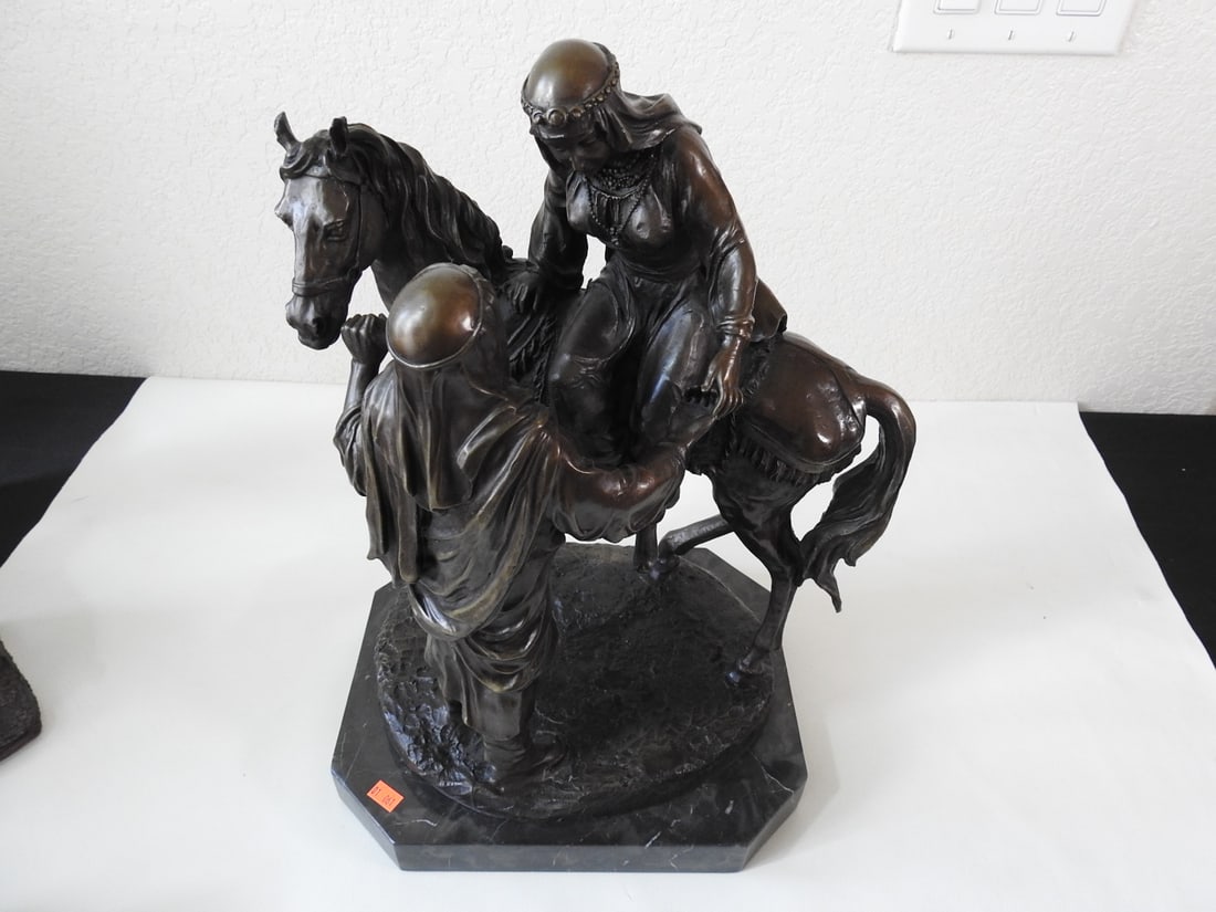 Bronze Arabian Man Assisting Woman Statue: Bronze figural statue depicting an Arabian man assisting a woman, mounted on a black marble base. Approx. 18 x 13 x 11 in.