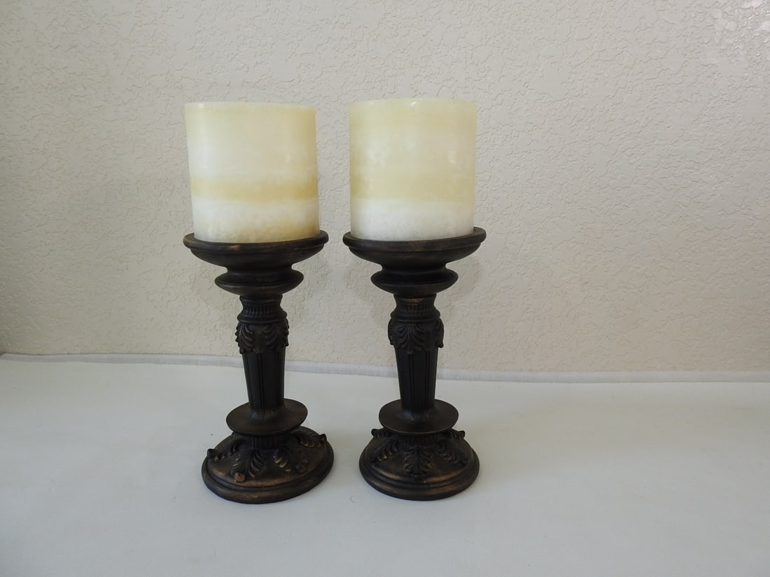 Pair of Roman Style Faux Bronze Candlesticks: Pair of Roman style faux bronze pillar candlesticks with acanthus leaf detail. Approx. 12.5 x 9.5 x 5 in.