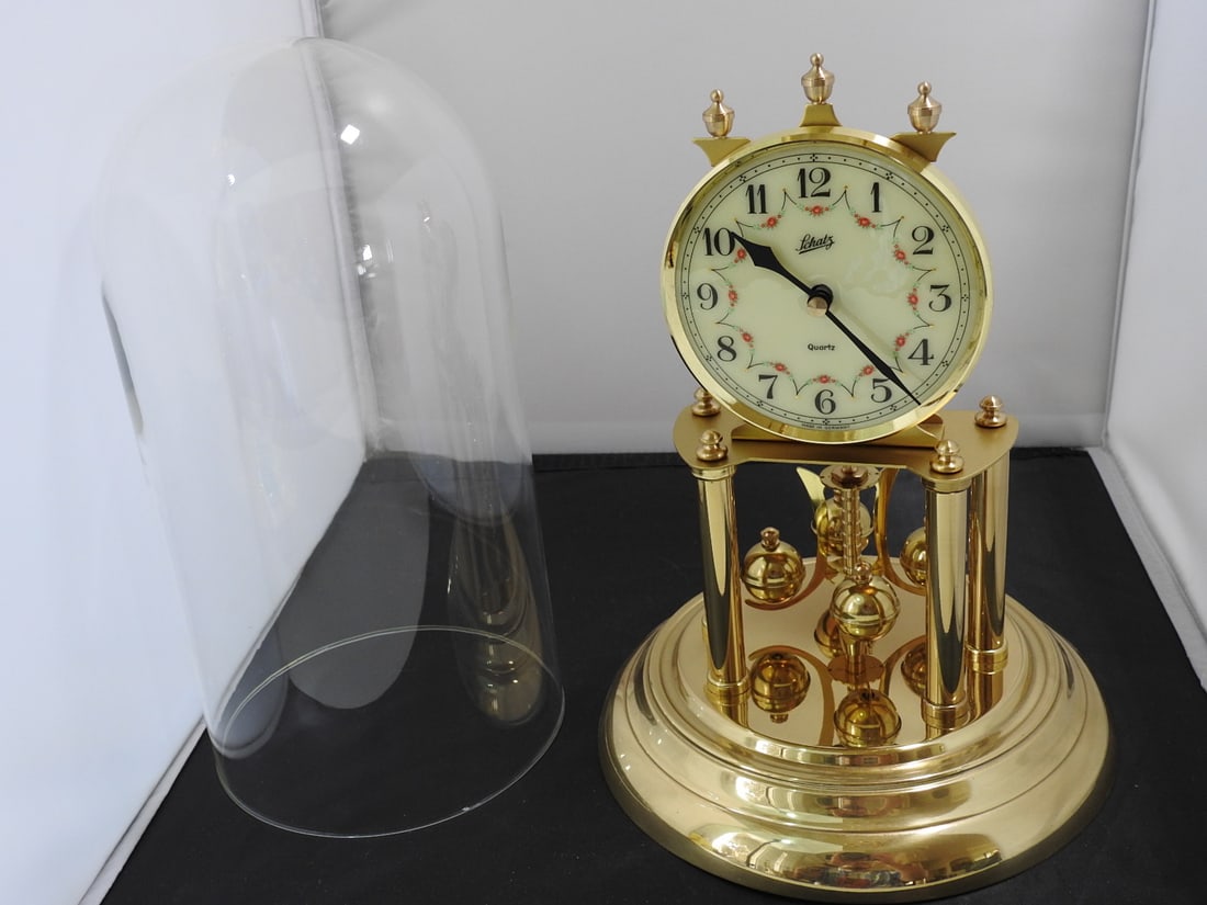 Brass-Tone Anniversary Style Mantel Clock Under Glass: Brass-tone anniversary style mantel clock under glass dome/case. Battery operated, made in China, with metal-coated plastic elements. Working per notes. Approx. 12 x 8 x 8 in.