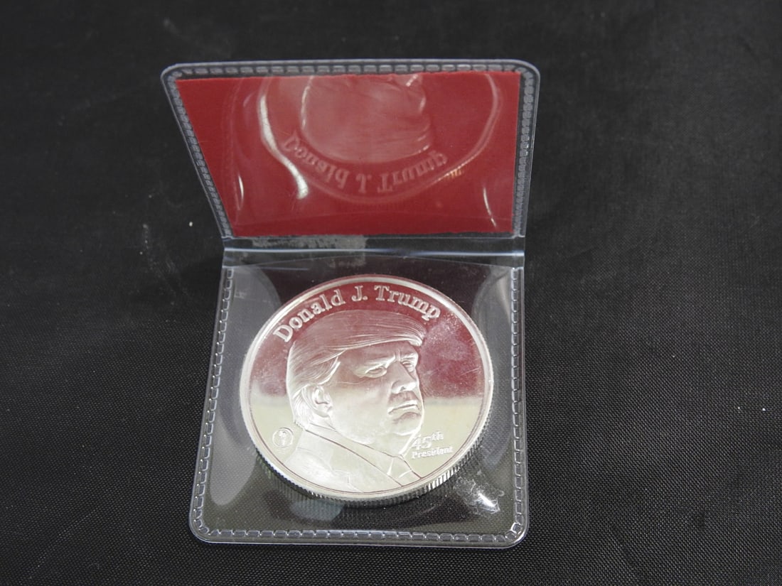 DJT Commemorative .999 Fine Silver Coin in Case: DJT commemorative coin in red presentation case, noted/marked as 1 troy oz .999 fine silver. Coin features raised architectural/White House-style design and portrait side as shown.