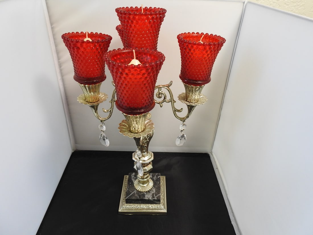 Four-Light Candelabra with Red Glass Votive Holders: Four-arm candelabra with red textured glass votive holders, antiqued gold finish over cast metal, black marble base, and original crystal prisms. Approx. 16.25 x 11 x 11 in.