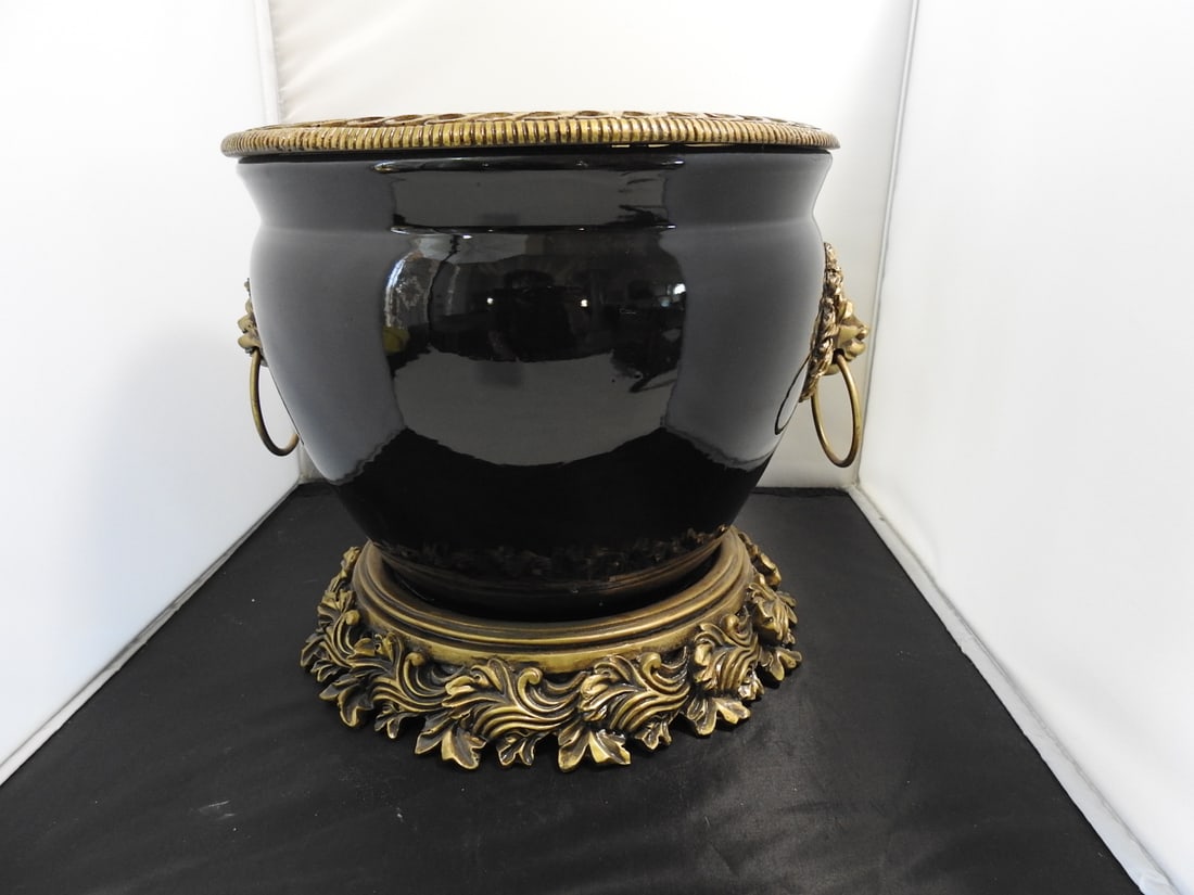 French Empire Style Black Flower Pot with Lion Heads: French Empire style black flower pot/cachepot with lion head ring handles, ornate gold-tone footed base, and ceramic/resin construction. Lightweight mass-produced decorative piece. Approx. 10.5 x 13 x