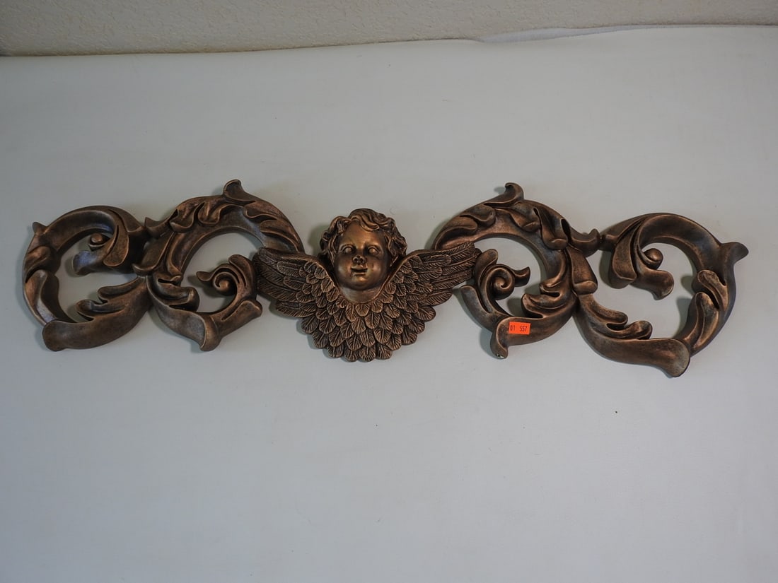 Gold Painted Cherub Wall Flourish: Large decorative cherub wall flourish in hard resin with painted gold finish and scroll/winged cherub design. Approx. 8.5 x 30 x 2.5 in.