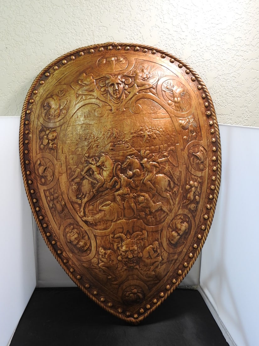 Design Toscano Faux Bronze Roman Parade Shield Wall Plaque: Design Toscano faux bronze Roman parade shield wall plaque in hollow resin, featuring raised classical battle scenes, mask detail, and decorative nailhead border. Back side has hanging holes and Desig