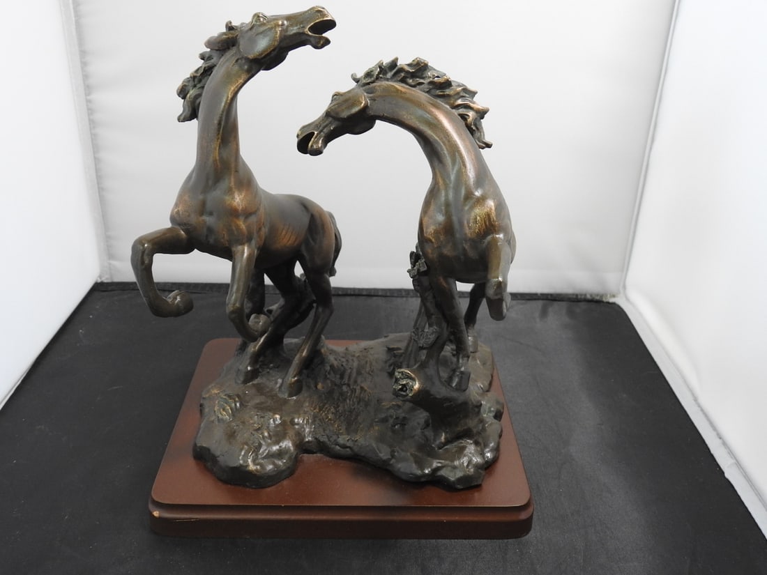 Faux Bronze Challenging Stallions Sculpture on Wood Base: Faux bronze Challenging Stallions sculpture depicting two rearing horses on a wooden base. Approx. 9.5 x 8 x 7 in.