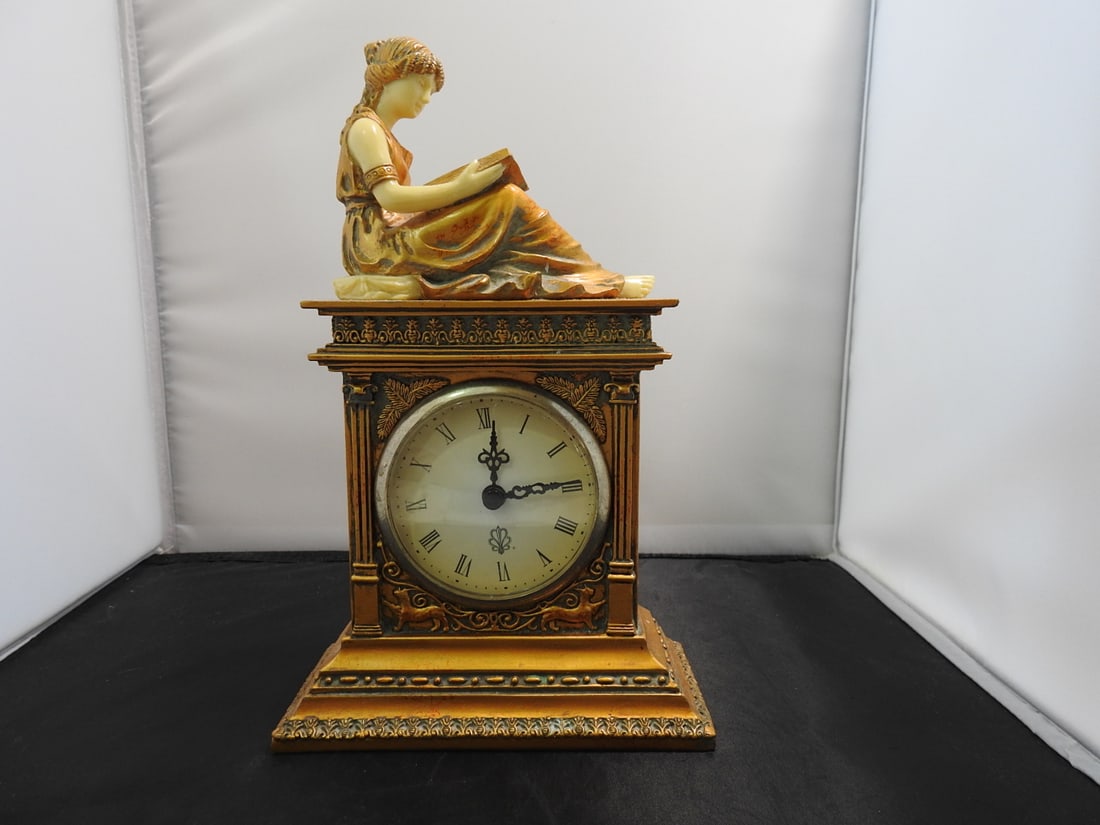 Taranus Reading Lady Mantel Clock: Reading Lady mantel clock signed Taranus, made of hard resin with gold-painted finish and inset clock face. Approx. 10 x 6.25 x 3.25 in.