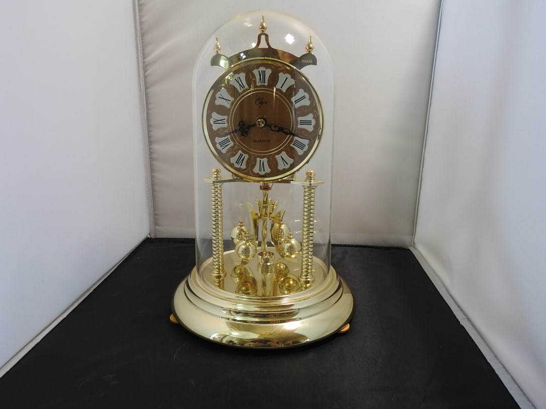 Brass Anniversary Style Mantel Clock with Dome: Brass anniversary style mantel clock with plastic dome/case, brass-tone rotating pendulum / carousel movement, plastic base, and chiming movement. Approx. 12.5 x 8 x 8 in.