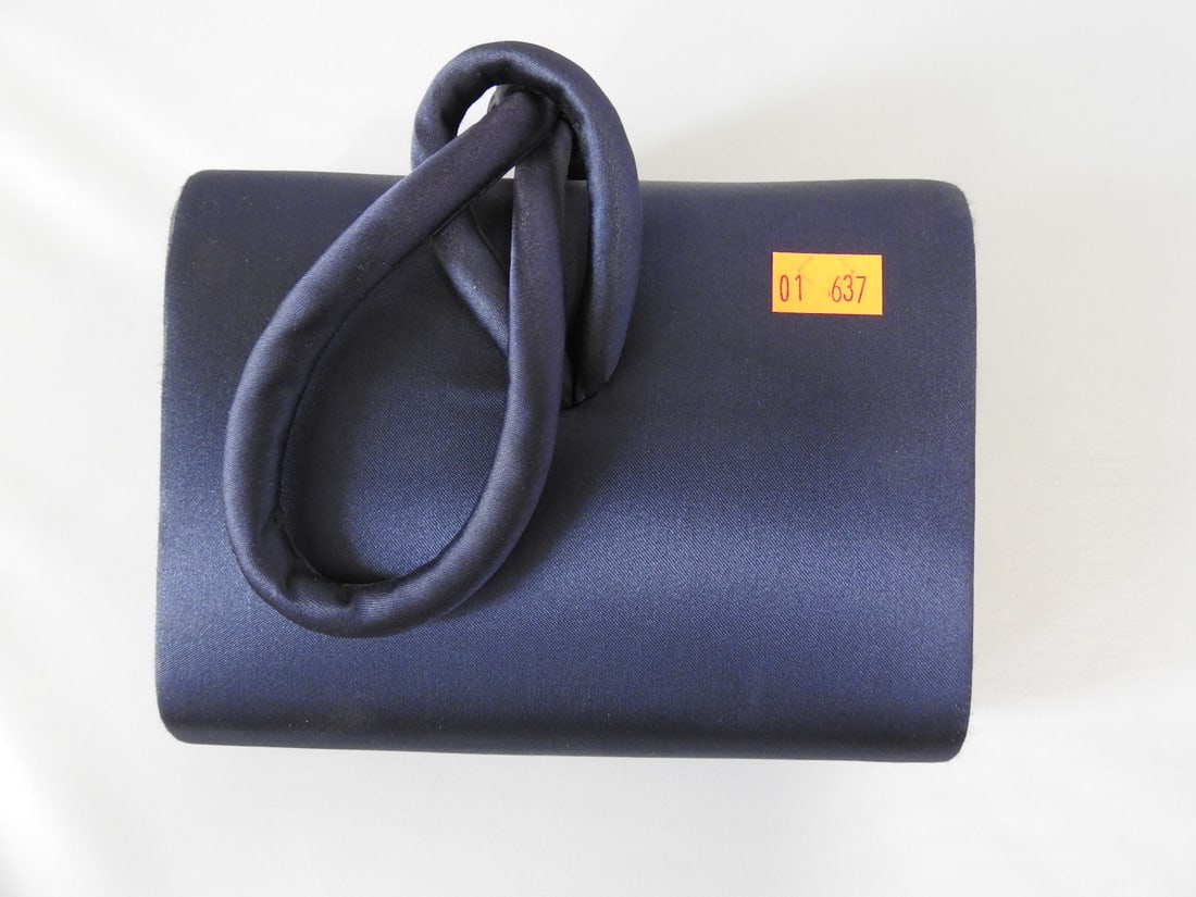 Valerie Stevens Blue Satin Clutch Bag: Valerie Stevens blue satin clutch bag with sculptural handle. Appears unused; one side shows apparent manufacturing defects. Approx. 6 x 6.25 x 2.25 in.