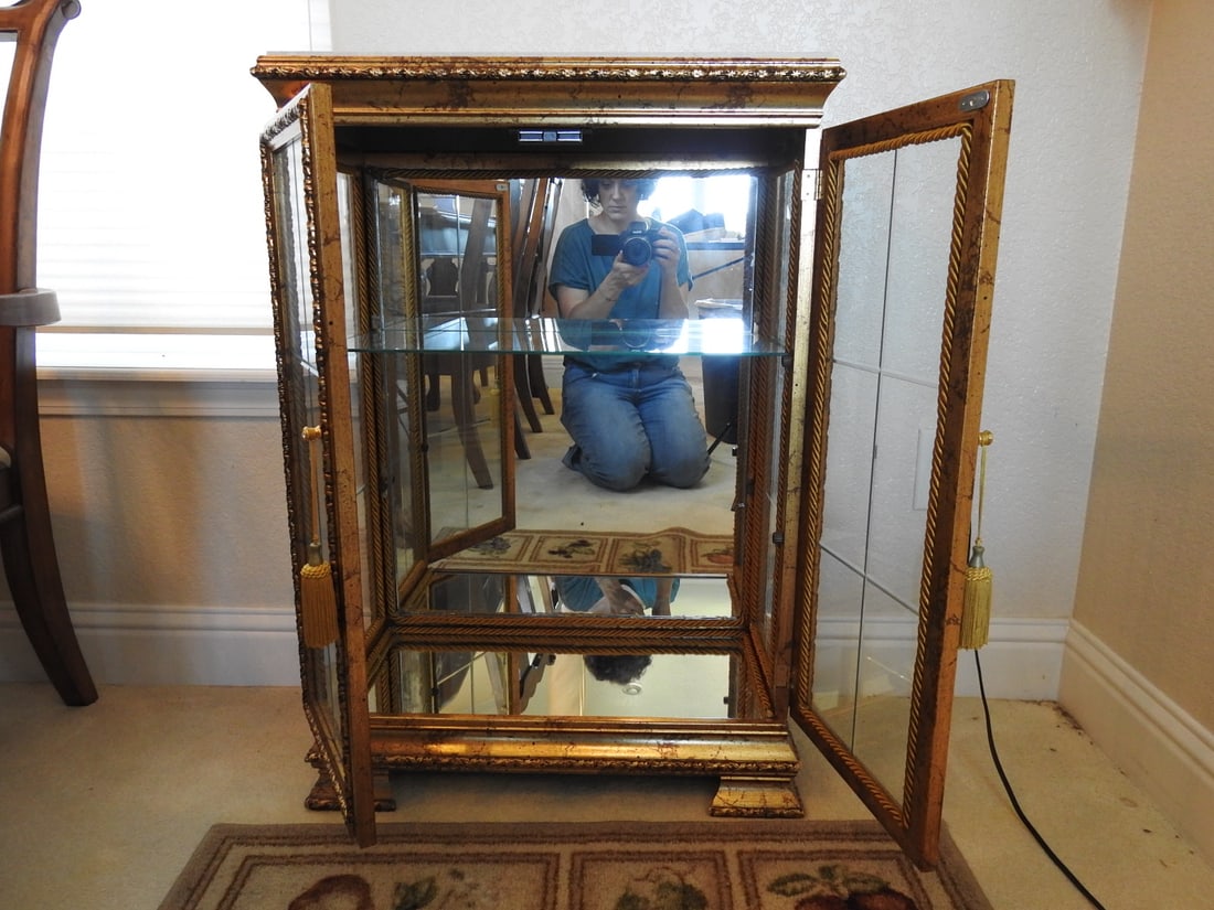 Venetian Rococo Revival Glass Display Cabinet: Venetian Rococo Revival style glass display cabinet with gold gilt wood frame, mirrored backing, glass shelves, beveled/edge glass doors, and faux marble top. Approx. 34.5 x 24 x 12 in.