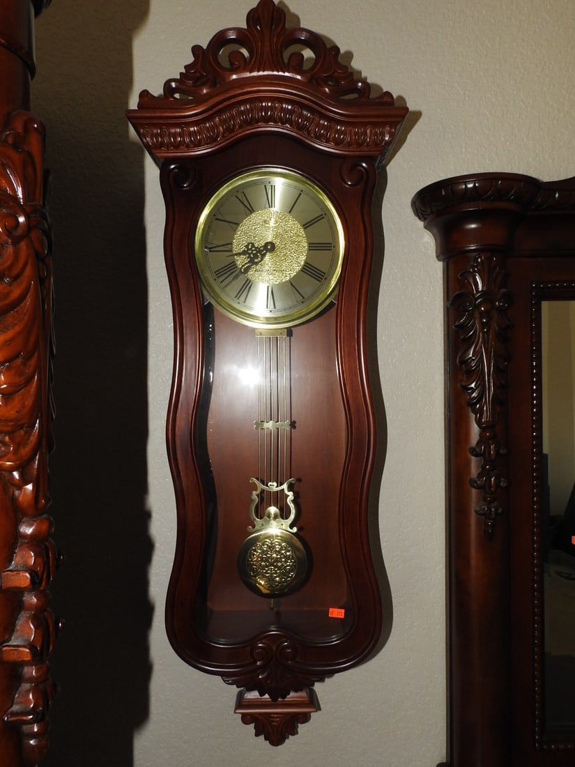 Vintage Cherry Finish Wall Clock: Vintage cherry finish wall clock with glass door, pendulum/weight-style decorative elements, and ornate carved-style cresting. Battery operated per notes. Approx. 41 x 14 x 7 in.