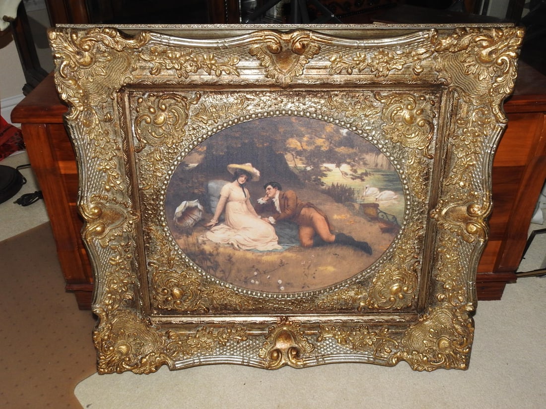 Lovers in the Park Ornate Framed Reprint: Decorative framed reprint depicting a romantic lovers-in-the-park scene, housed in an ornate gilt frame. Approx. 28.75 x 33 x 3.5 in.