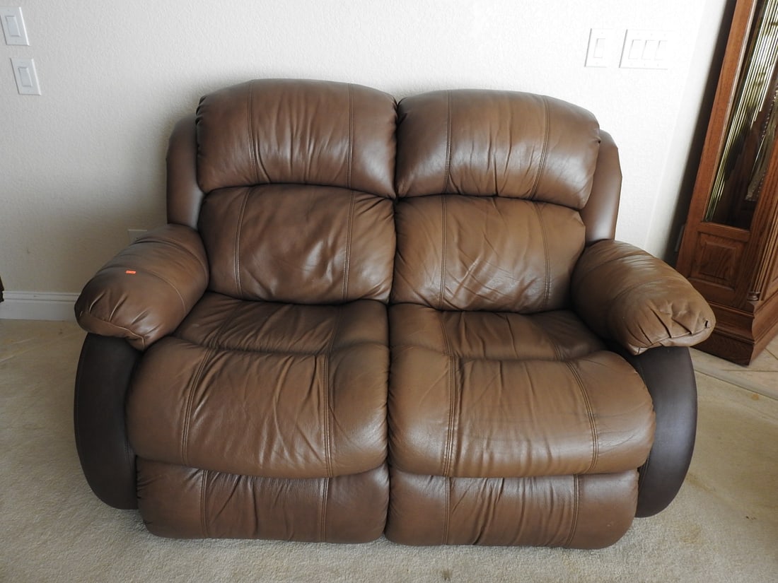 McGann Brown Leather Manual Reclining Loveseat: McGann brown leather reclining loveseat with dual reclining seats, padded arms, and plush back cushions. Manual recliner per notes. Approx. 40 x 64 x 46 in.