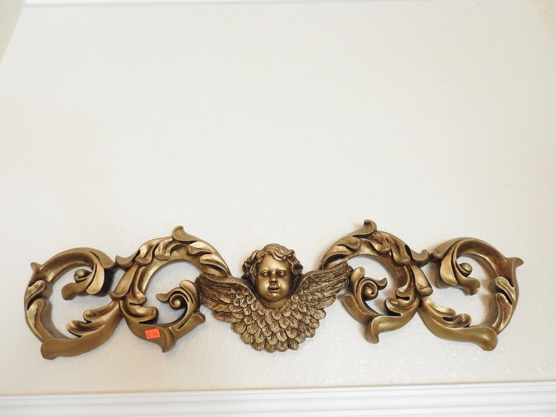 Gold Painted Cherub Wall Flourish: Large decorative cherub wall flourish in hard resin with painted gold finish, winged cherub center, and scrollwork design. Approx. 8.5 x 30 x 2.5 in.