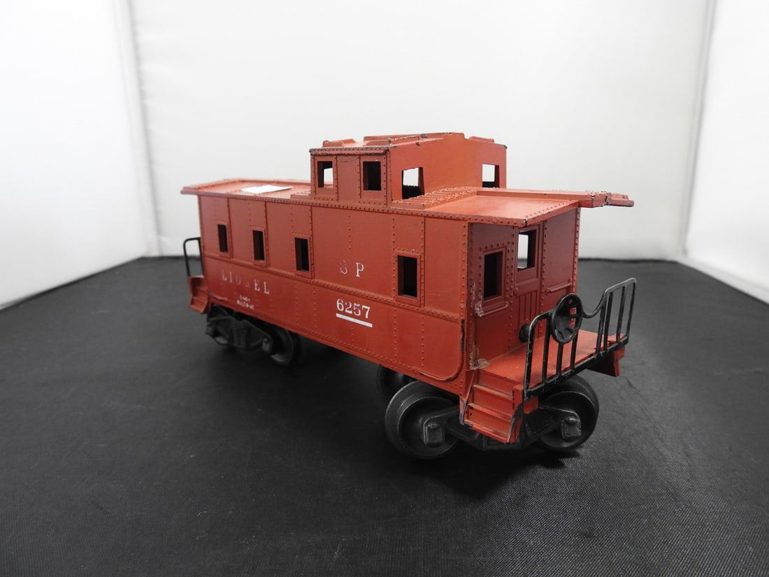Lionel No. 6257 Southern Pacific Caboose: Lionel O gauge No. 6257 Southern Pacific caboose with red/brown body, SP markings, end platforms, ladders, and black handrails. Postwar-era, 1950s-style caboose with visible paint wear. Approx. 3.5 x