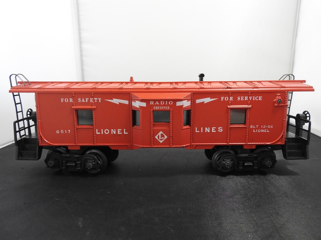 Lionel No. 6517 Bay Window Caboose: Lionel O gauge No. 6517 Lionel Lines bay window caboose in red/orange with 'For Safety / For Service' and 'Radio Equipped' markings, end platforms, and black trucks. Side lettering includes BLT 12-55