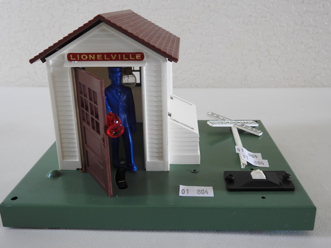 Lionel Automatic Flagman / Railroad Crossing Accessory: Lionel automatic flagman / railroad crossing accessory with Lionelville shed, crossing sign, and flagman figure. Notes indicate the crossing is broken. Vintage / postwar-style Lionel layout