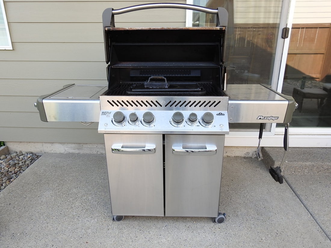 Napoleon Prestige Stainless Steel Propane Gas Grill: Napoleon Prestige stainless steel propane gas grill with Sizzle Zone side burner, Accu-Probe hood thermometer, cast iron cooking plates/grates, cabinet base, side shelves, propane tank, and
