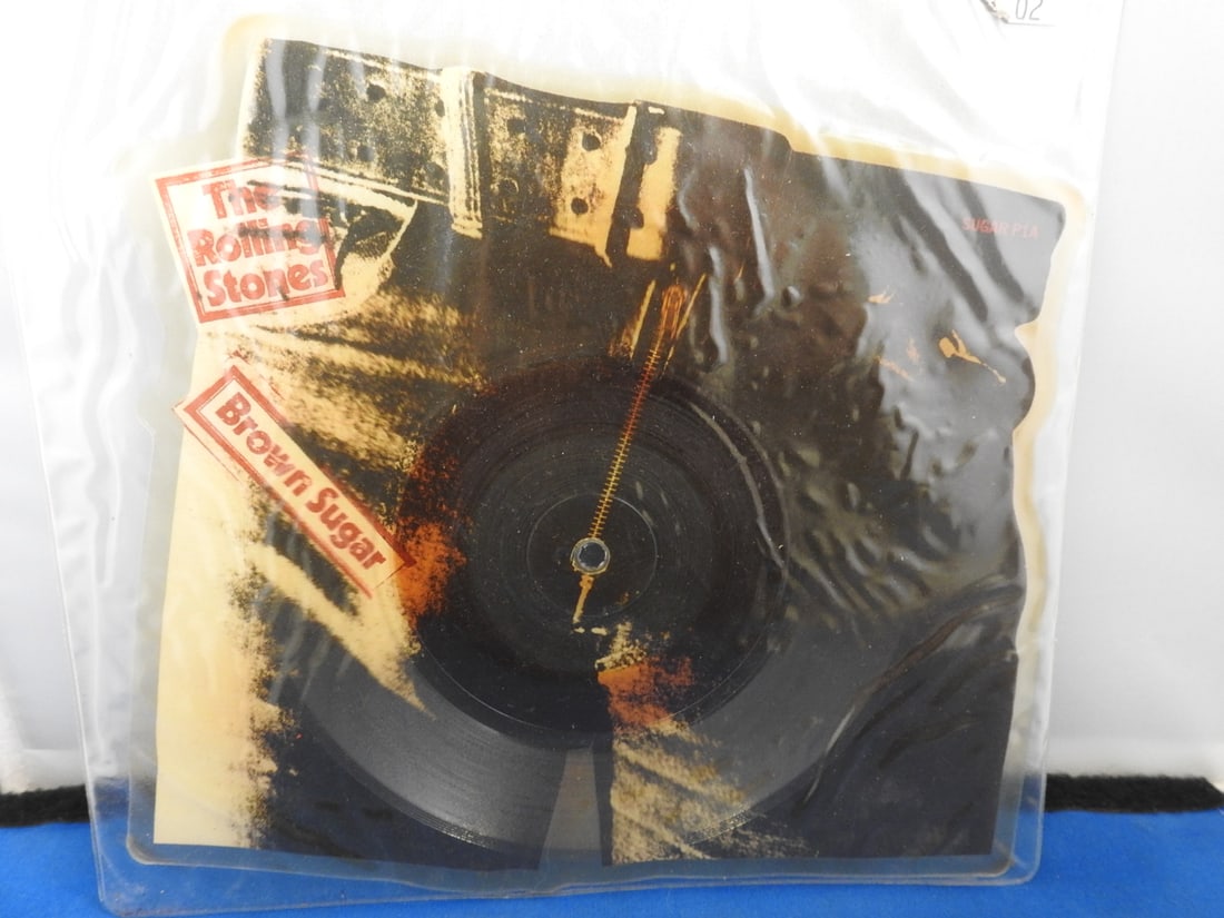 The Rolling Stones Brown Sugar Pants-Shaped Picture Disc: The Rolling Stones Brown Sugar pants-shaped picture disc in clear plastic packaging, featuring jeans imagery and a Brown Sugar / Bitch label sticker as photographed.