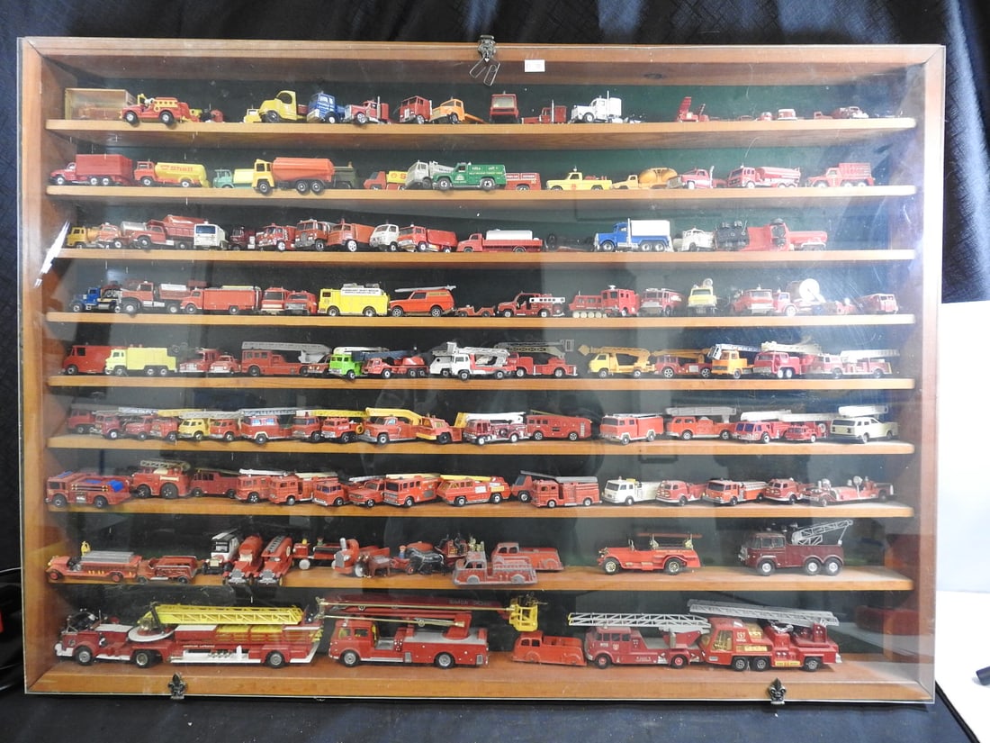 Large Display Case of Die-Cast Fire and Emergency Vehicles: Wood and clear-front display case containing an extensive collection of die-cast fire, rescue and emergency vehicles in mixed scales. Visible makers include Matchbox and others; exact count has not