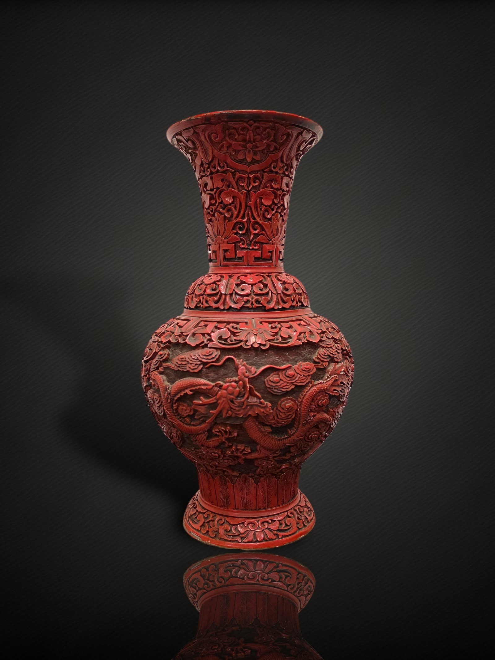 A Chinese Carved Cinnabar Lacquer 'Dragon' Baluster Vase: A baluster vase worked in thick cinnabar-red lacquer and carved in deep relief. The globular body is decorated with a sinuous, scaly dragon writhing amid dense ruyi-cloud scrolls in pursuit of a flami
