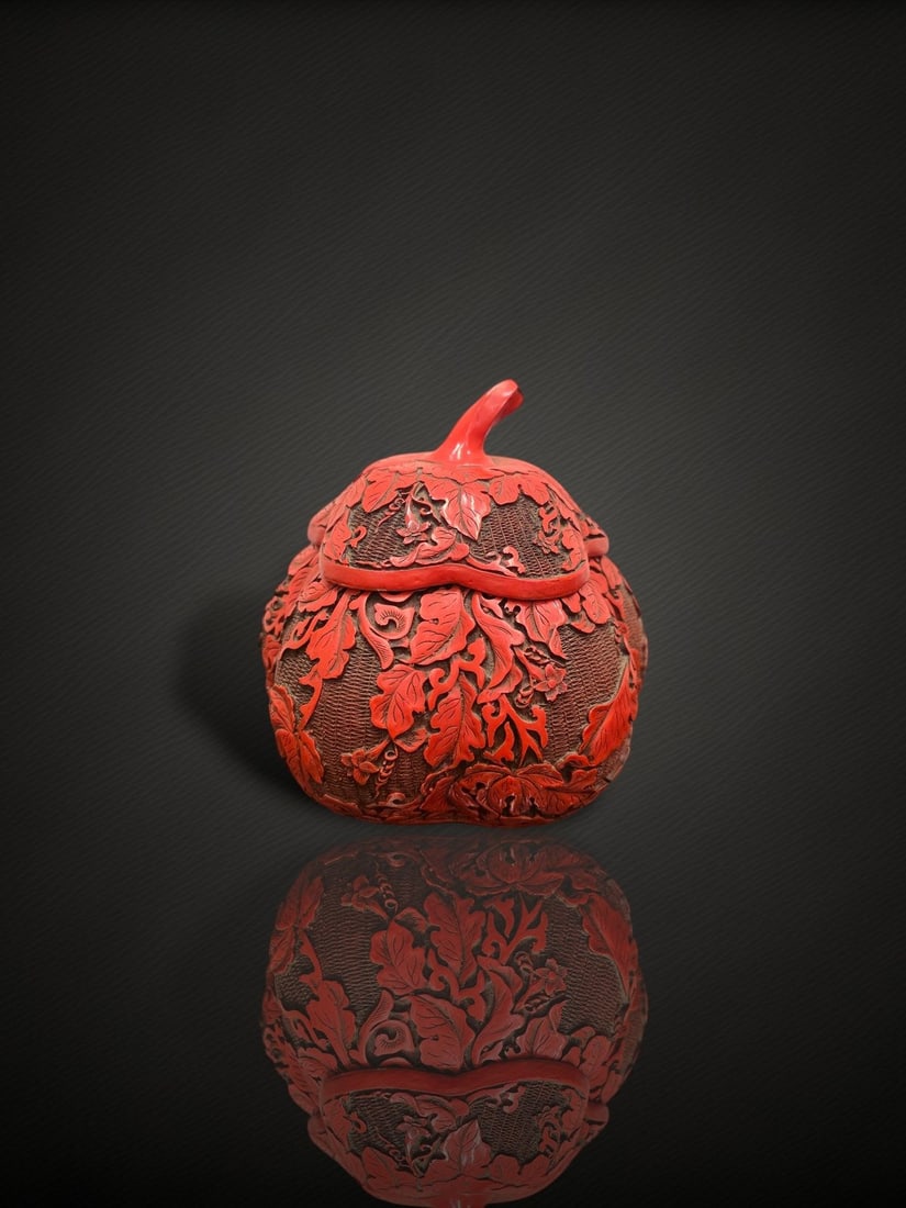 A Chinese Carved Cinnabar Lacquer 'Gourd' Box and Cover: A carved cinnabar lacquer box and cover modelled in the form of a gourd or fruit, the domed cover surmounted by a curling stem finial and carved in relief with trailing leafy vines, foliage and blosso