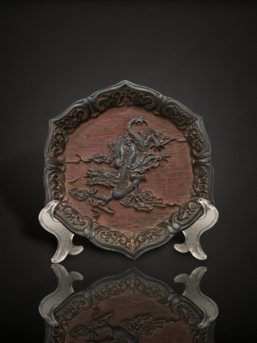 A Chinese Carved Lacquer 'Immortal and Dragon' Dish: A carved lacquer dish of foliate form, the surface of dark brown to near-black tone, decorated in relief with a robed immortal or scholar figure standing amid scrolling clouds beside a writhing dragon