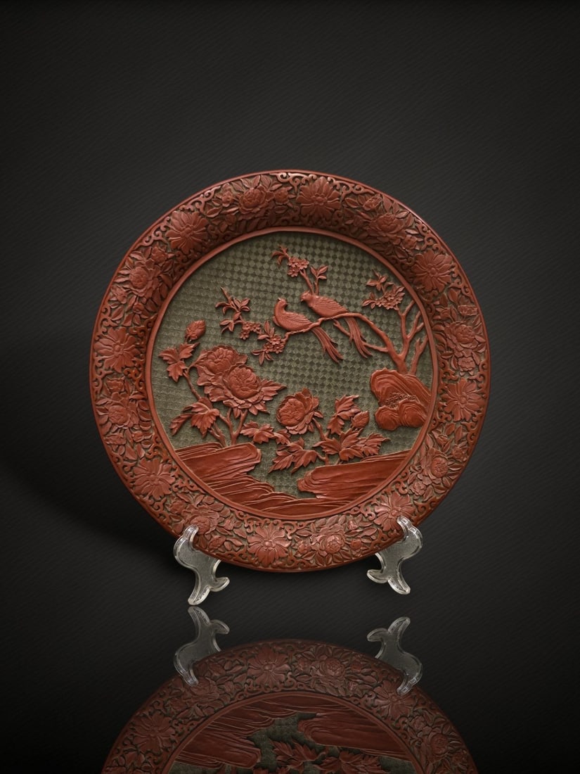A Chinese Carved Two-Colour Lacquer 'Birds and Peony' Dish: A circular dish carved in red lacquer against a contrasting green diaper ground, the central medallion depicting a pair of long-tailed birds perched upon a flowering branch above blossoming peonies gr