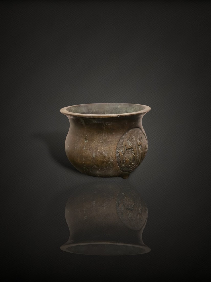 A Chinese Bronze 'Arabic Inscription' Censer: A cast bronze incense burner of compressed bombe form, rising from a short foot to a slightly waisted neck and everted rim, supported on small feet. The rounded body is cast in low relief with roundel