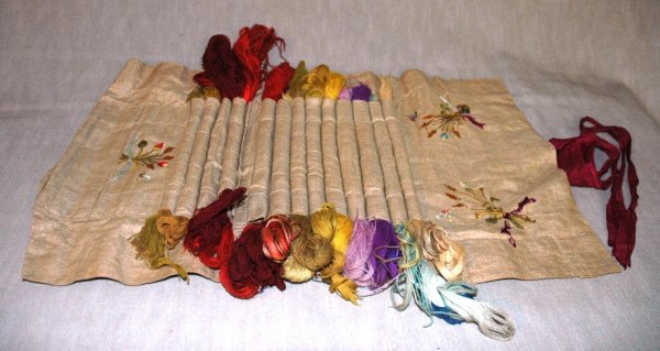 A FRENCH EMBROIDERY'S APRON, 19th Century, made of: A FRENCH EMBROIDERY'S APRON, 19th Century, made of silk embroidered linen with fourteen segments holding various colored skenes of Aubusson wool and closing with a burgundy silk ribbon, length 20 1/2"