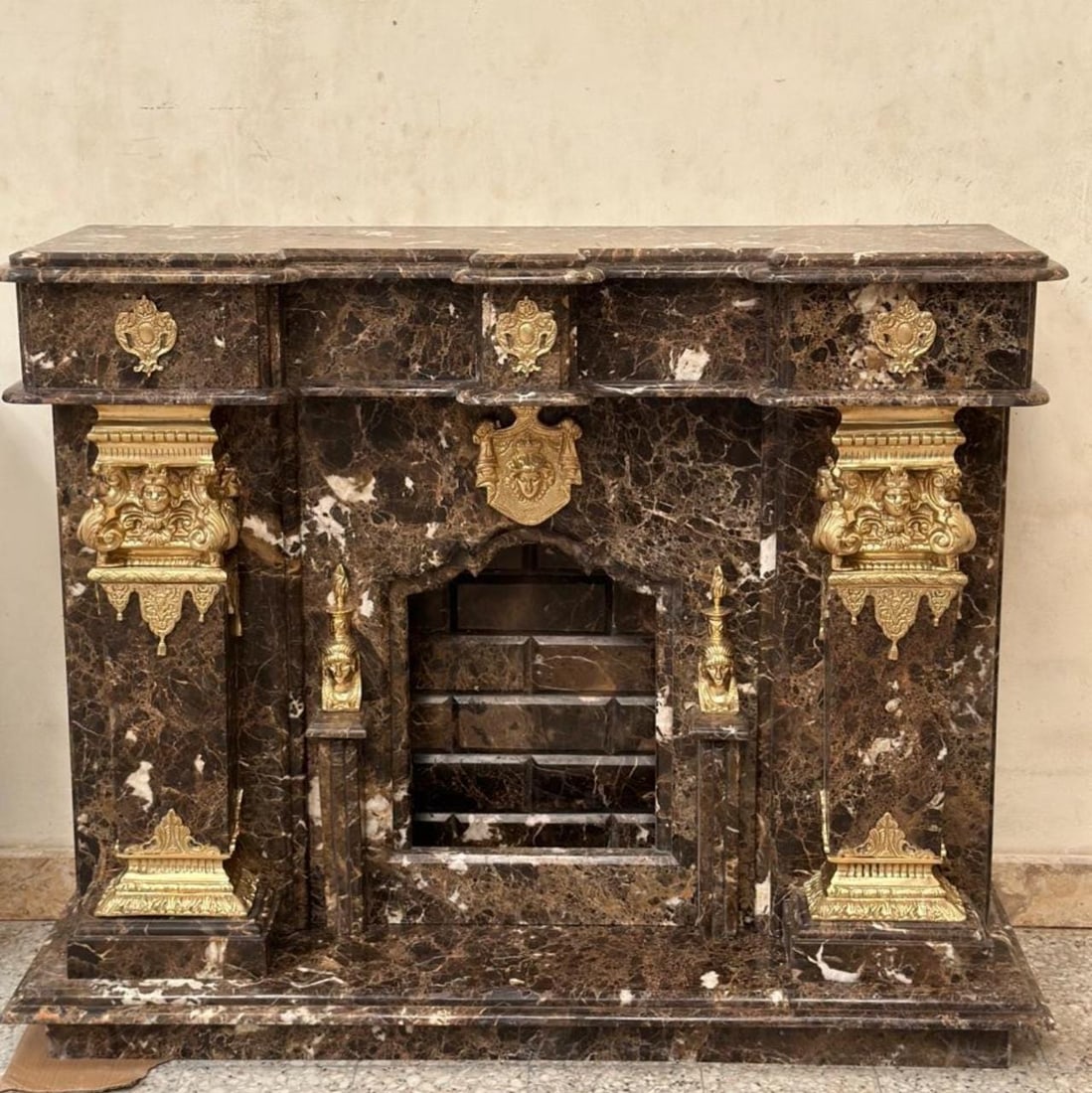 Black Marble Fireplace Mantel – Gold Corinthian: Description: Add grandeur and timeless style to your space with this exceptional Neoclassical-style fireplace mantel, meticulously crafted from richly veined marble. Featuring bold natural streaks acr