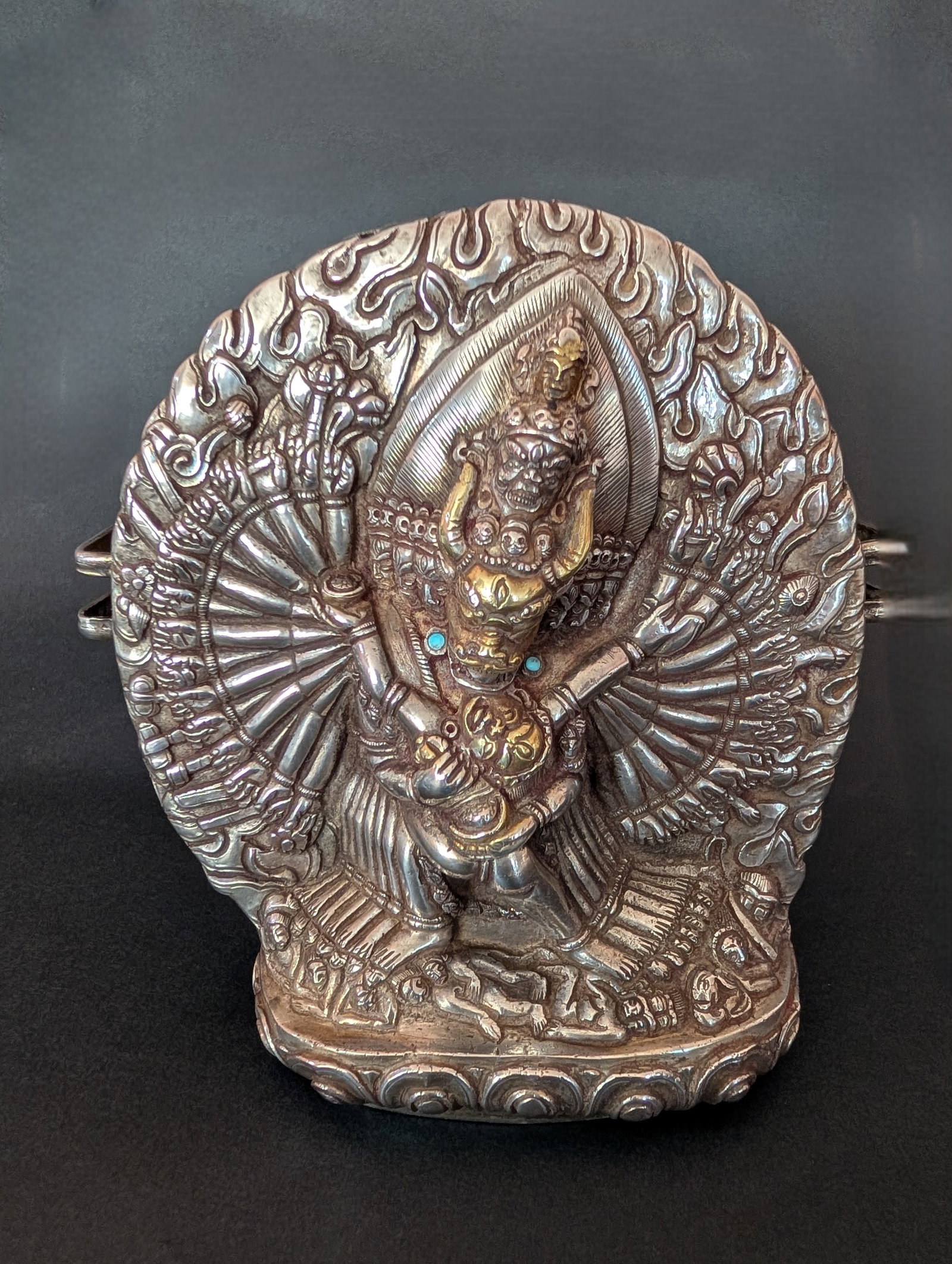 Parcel Gilt Silver Repousse Gau Depicting Vajrabhairava and Consort, Bhutan, 19th c: A finely chased and embossed silver cover on this large Gau with Parcel-Gilt faces and turquoise earrings set in a bezel. Vajrabhairava is a wrathful form of Manjushri. He is not a protector deity but