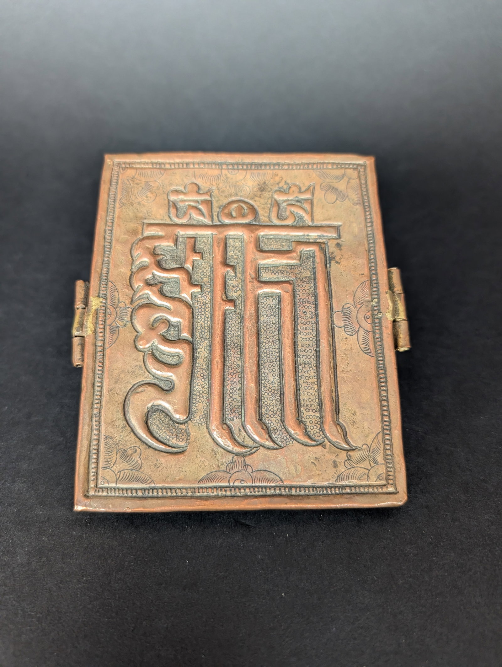 Kalachakra Gau, Copper alloy repousse: The Kalachakra symbol in Lantsa script is depicted on this unusually slim Gau. It is only half an inch thick. A border of stamped decorative floral features is dedicated to the central script. The