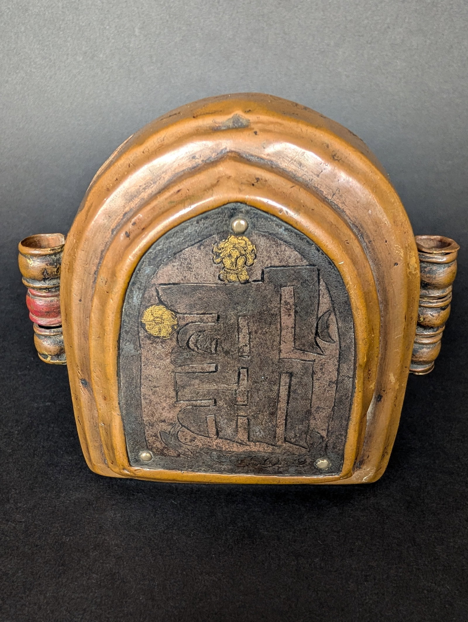 Copper Gau with Namchu Wangden Mantra in iron and gold: The softly pointed niche-shaped Gau has a raised shrine-like addition on the front, which houses the iron plate holding the symbol Namchu Wangden, signifying The One with Ten Powers. It contains the
