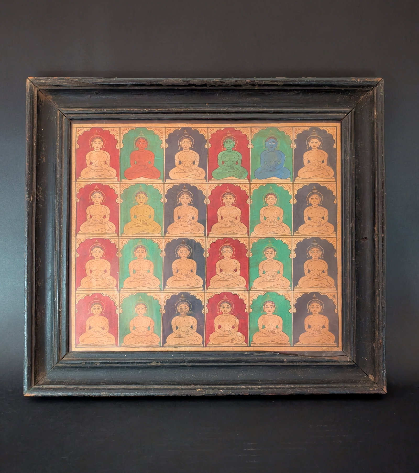 24 Seated Tirthankara painting, 19th century: The series of 24 tirthankaras in four rows is hand painted in polychrome, possibly gouache and gold which has faded over the years. Each Tirthankara is seated in an arched frame without individual lan
